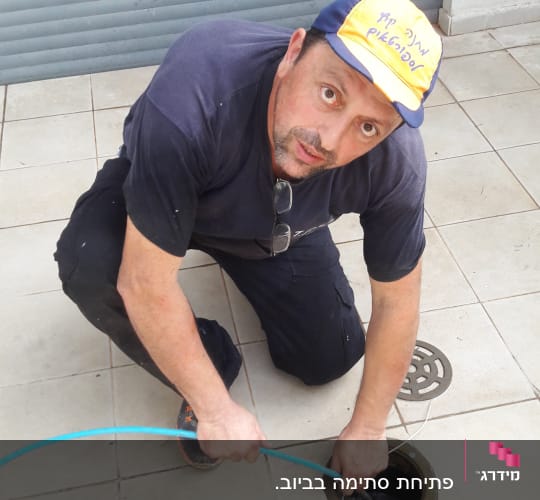 אדם עובד עם צינור ניקוז בפתח ביוב
